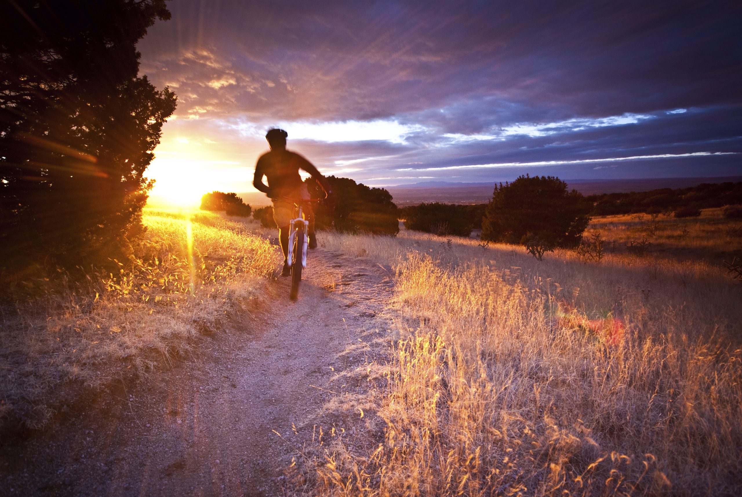 A cyclist riding a cycle on a trail during sunset